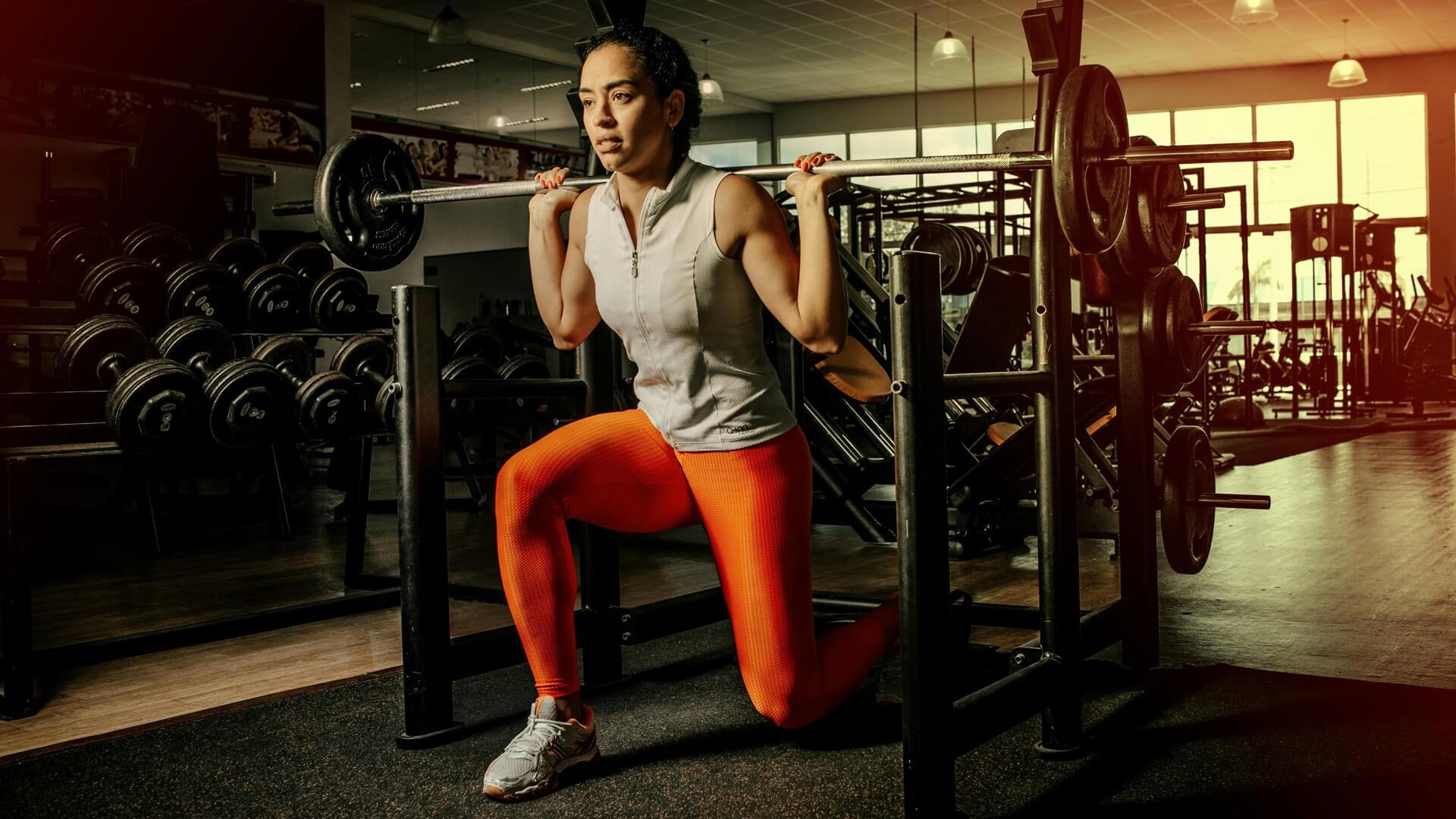 a female doing squat with barbell and weights at gym