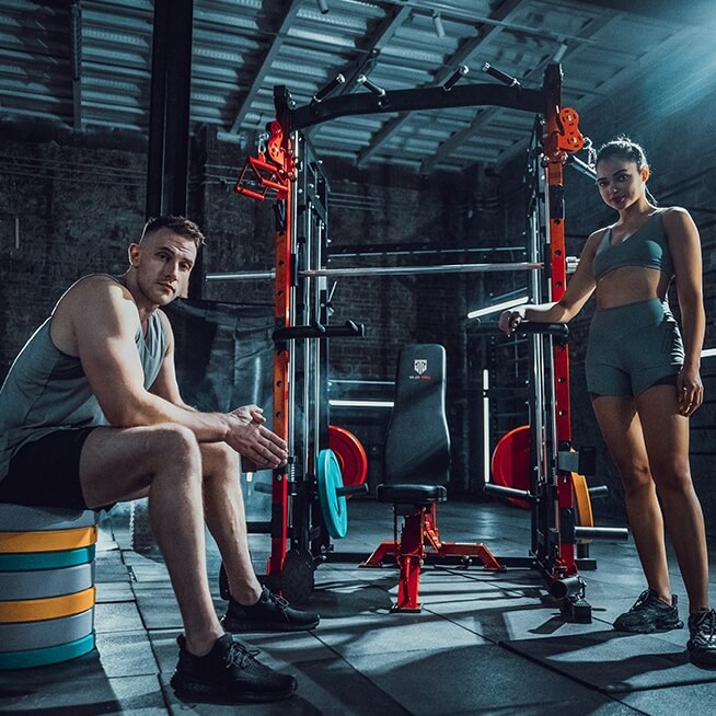 man and woman in gym with smith machine