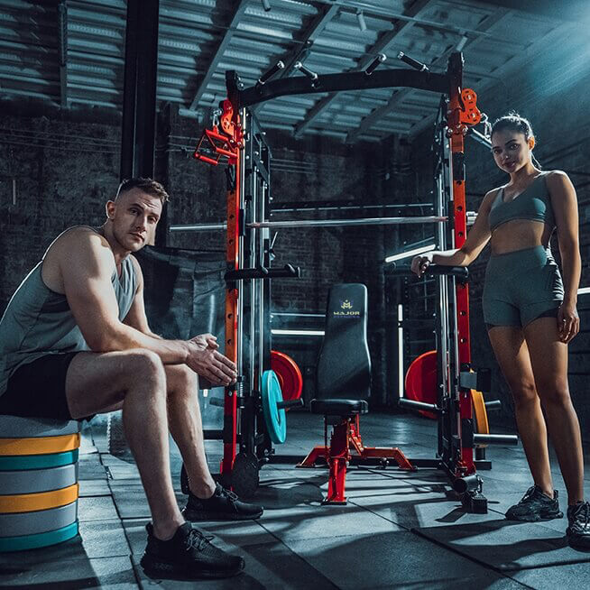 A man and woman standing in front of a Major Fitness Smith machine taking a break.
