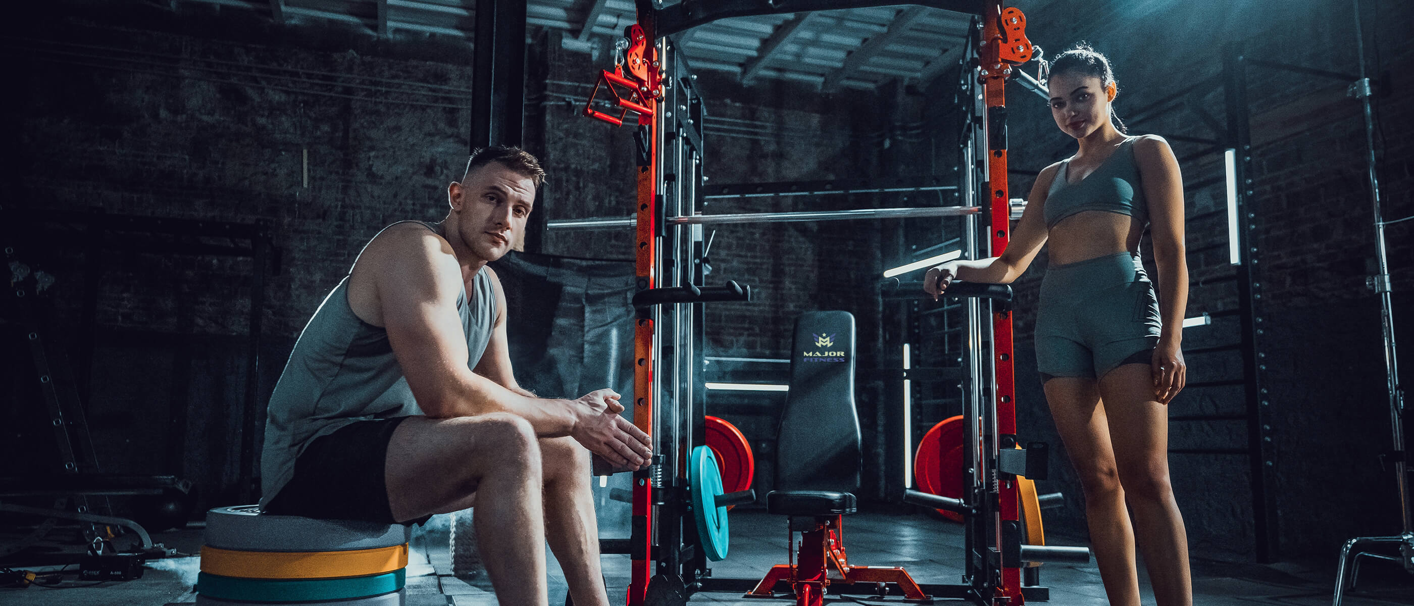Focused man and woman in athletic gear training in a rustic brick-walled home gym, featuring a Major Fitness power rack.