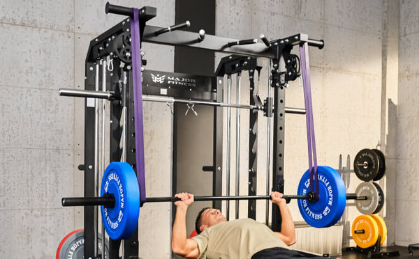 man performing a bench press on a Smith machine  by using purple resistance bands