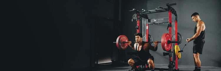 Dynamic fitness scene with two male athletes in a well-equipped Major Fitness home gym. One performs a barbell squat using a red and black power rack, while the other engages in a focused cable workout